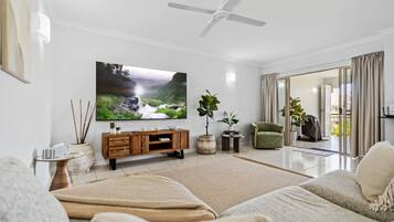 A modern living room with a flat-screen TV, a ceiling fan, a green armchair, and a sliding glass door leading to an outdoor area.