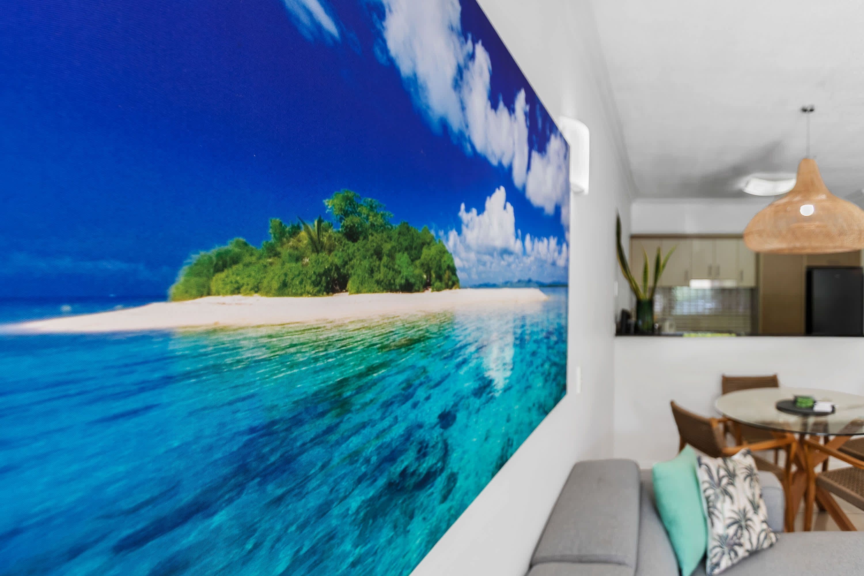 A living room with a large wall mural of a beach scene, a dining area with a round table and chairs, and a hanging pendant light.