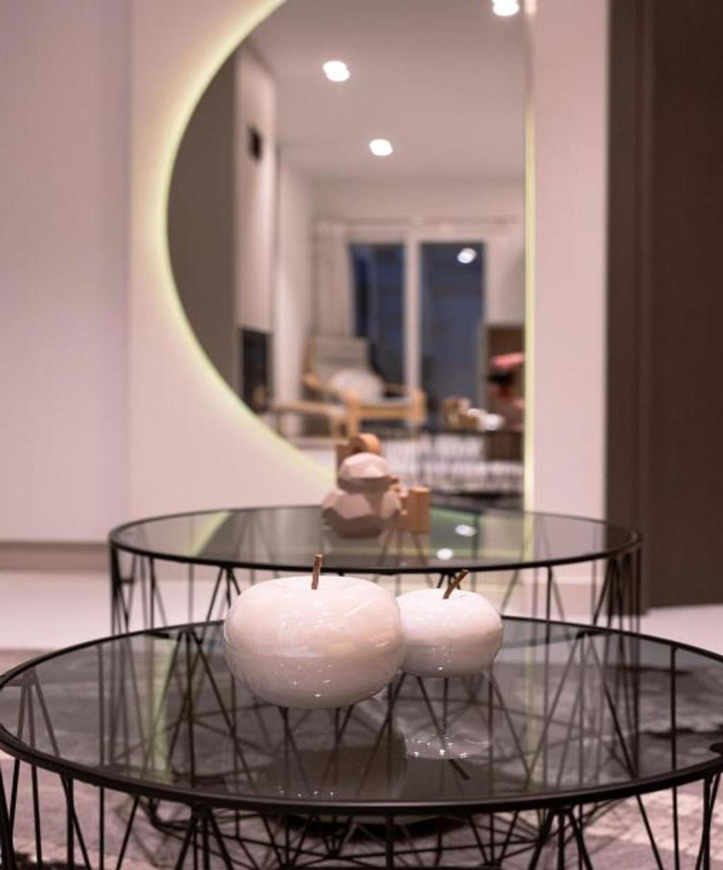 A round glass table with a wireframe base, three spherical objects on it, and a mirror reflecting a room with a bed and a window.