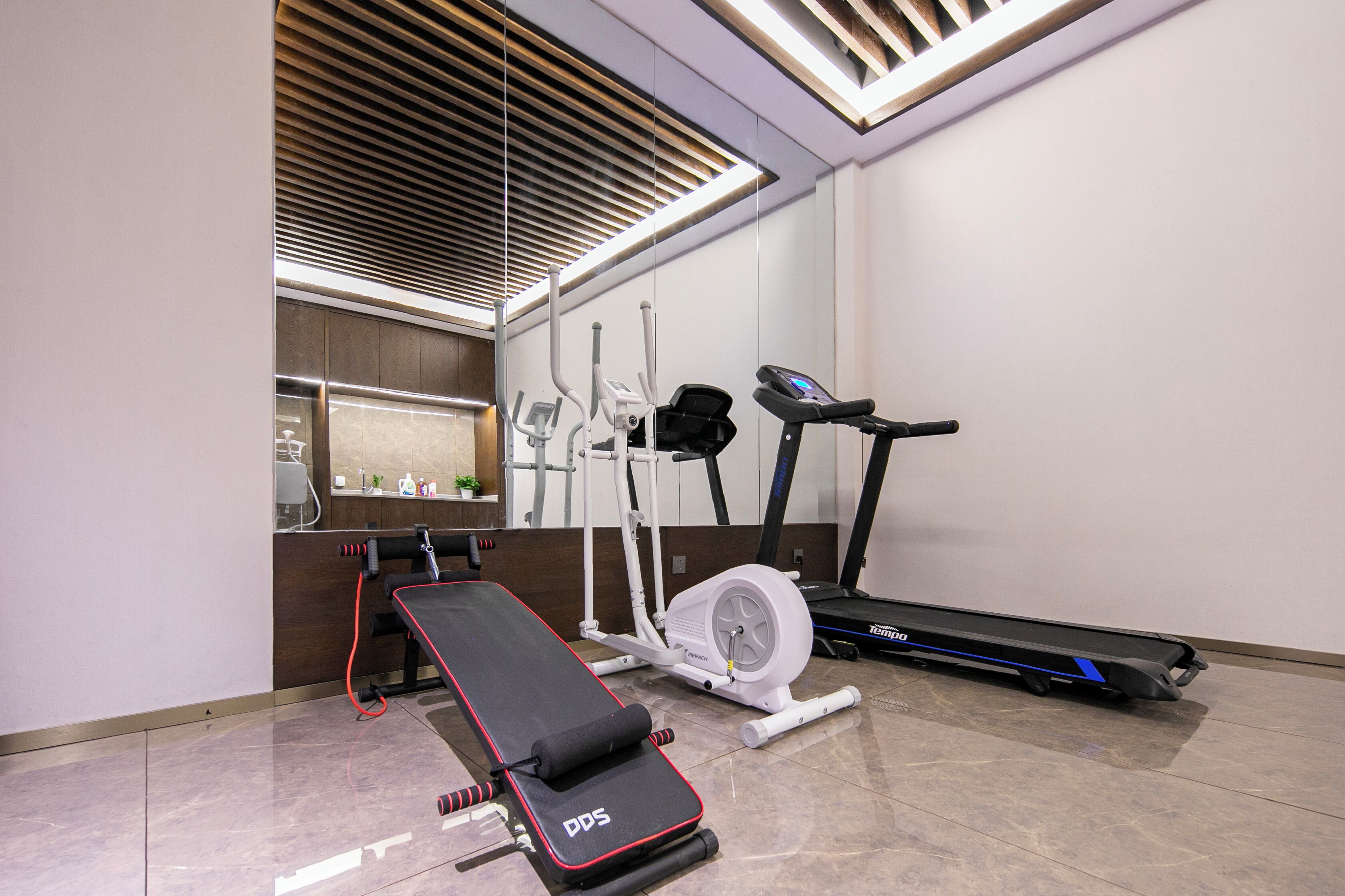 A gym with a treadmill, elliptical, and a bench press.