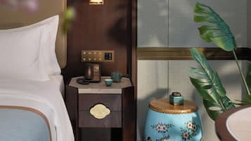 A hotel room with a bed, bedside table with a lamp, a telephone, and a decorative plant.