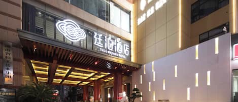 A hotel entrance with a modern design, featuring a prominent illuminated sign and a covered entrance area.