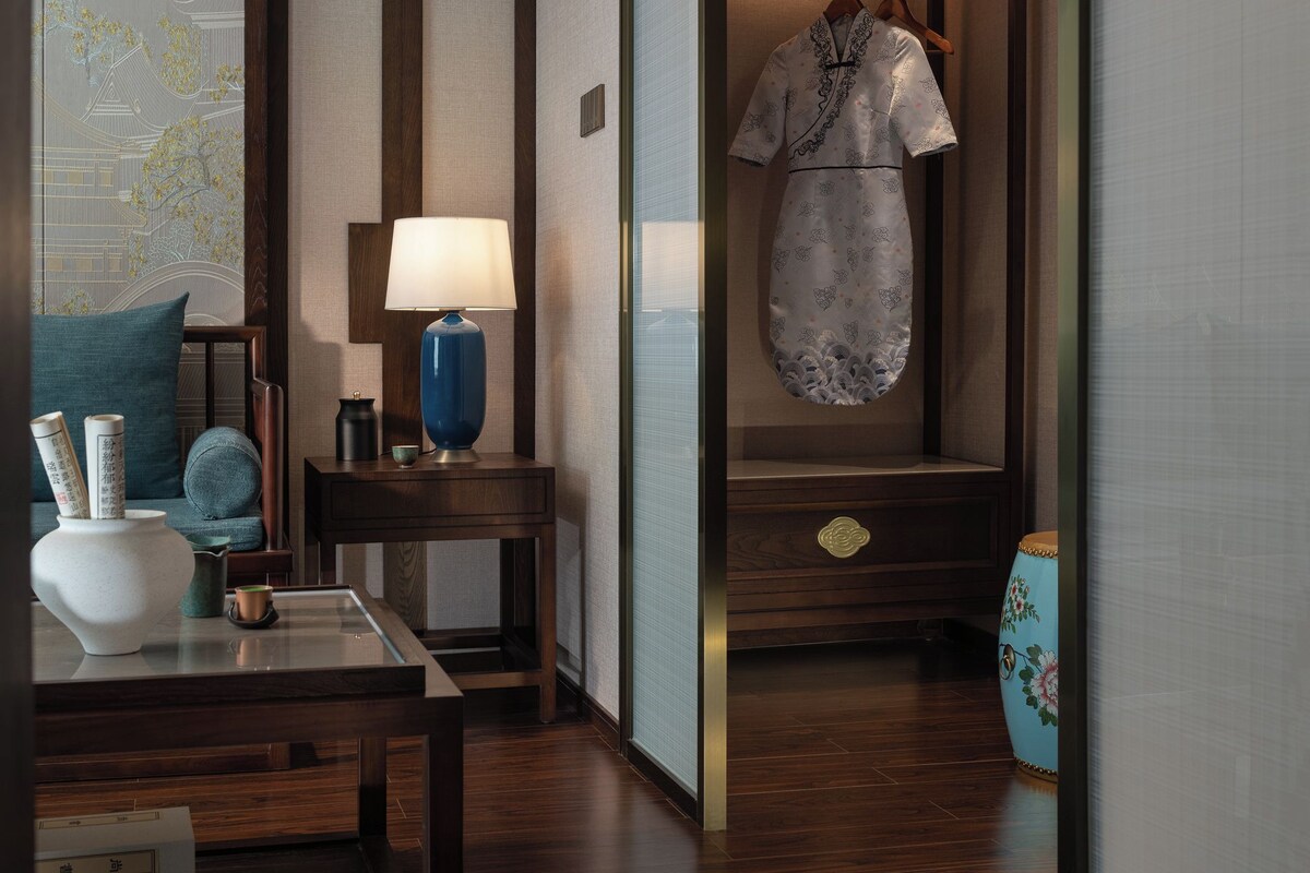 Una habitación japonesa tradicional con suelo de madera, una mesa con lámpara, una prenda colgada y un jarrón decorativo.