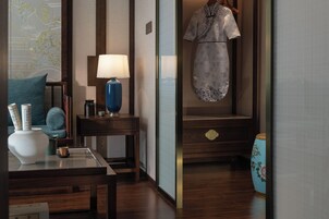 A traditional Japanese room with a wooden floor, a table with a lamp, a hanging garment, and a decorative vase.