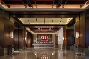 A modern lobby with a reception desk, wooden paneling, and a polished marble floor.