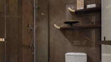 Un baño moderno con ducha de mampara de vidrio, inodoro y repisa con artículos de aseo.