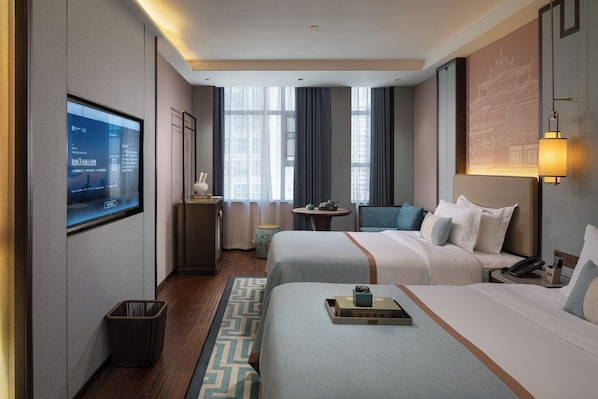 A hotel room with two beds, a TV, a small table with a teapot, and a decorative lamp.