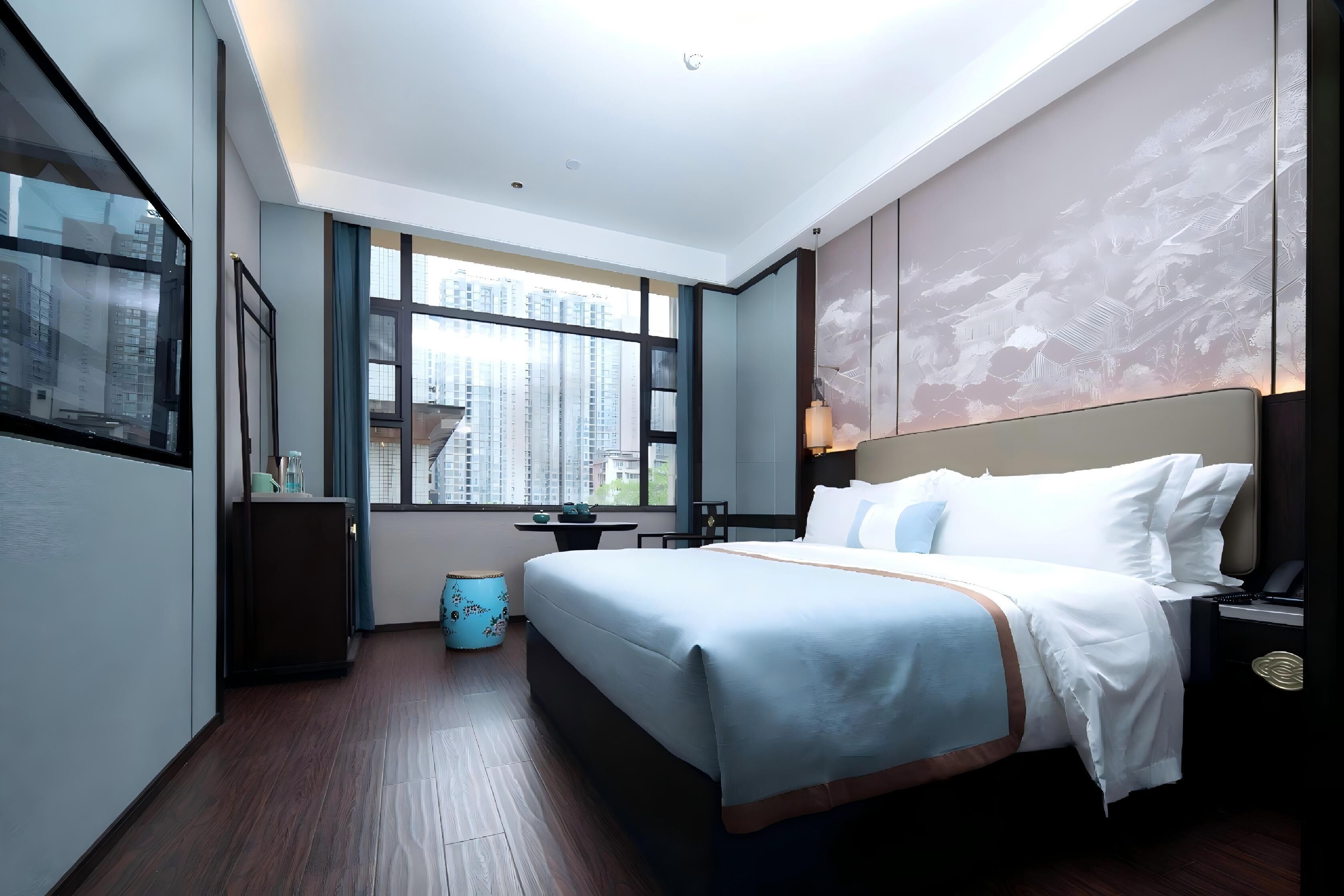 Une chambre d’hôtel moderne avec un grand lit, un bureau et une vue sur de hauts immeubles.