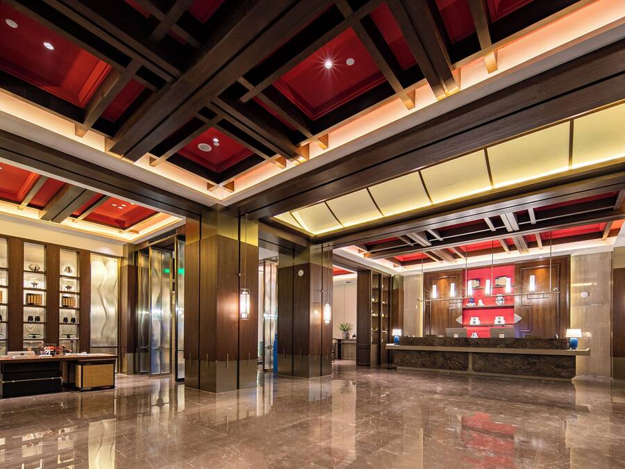 A modern lobby with a polished marble floor, wooden paneling, and a reception desk with a red accent wall.