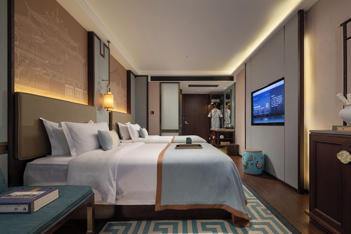 Habitación de hotel con dos camas, un televisor, un armario y un adornado cabecero.