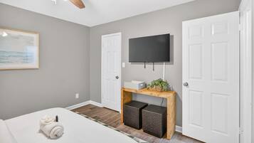 A bedroom with a bed, a ceiling fan, a mounted TV, and a door.
