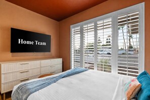 A bedroom with a bed, a TV mounted on the wall, a dresser, and a window with blinds. - Golf Simulator Pool Sports Court Sleeps 24 (Mesa)