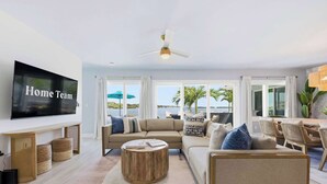 A living room with a large flat-screen TV, a ceiling fan, a sofa, a coffee table, and a dining area with chairs and a table. - Private Dock Pool Hot Tub Puttputt Games (St. Petersburg)