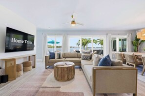 A living room with a large flat-screen TV, a ceiling fan, a sofa, a coffee table, and a dining area with chairs and a table. - Private Dock Pool Hot Tub Puttputt Games (St. Petersburg)
