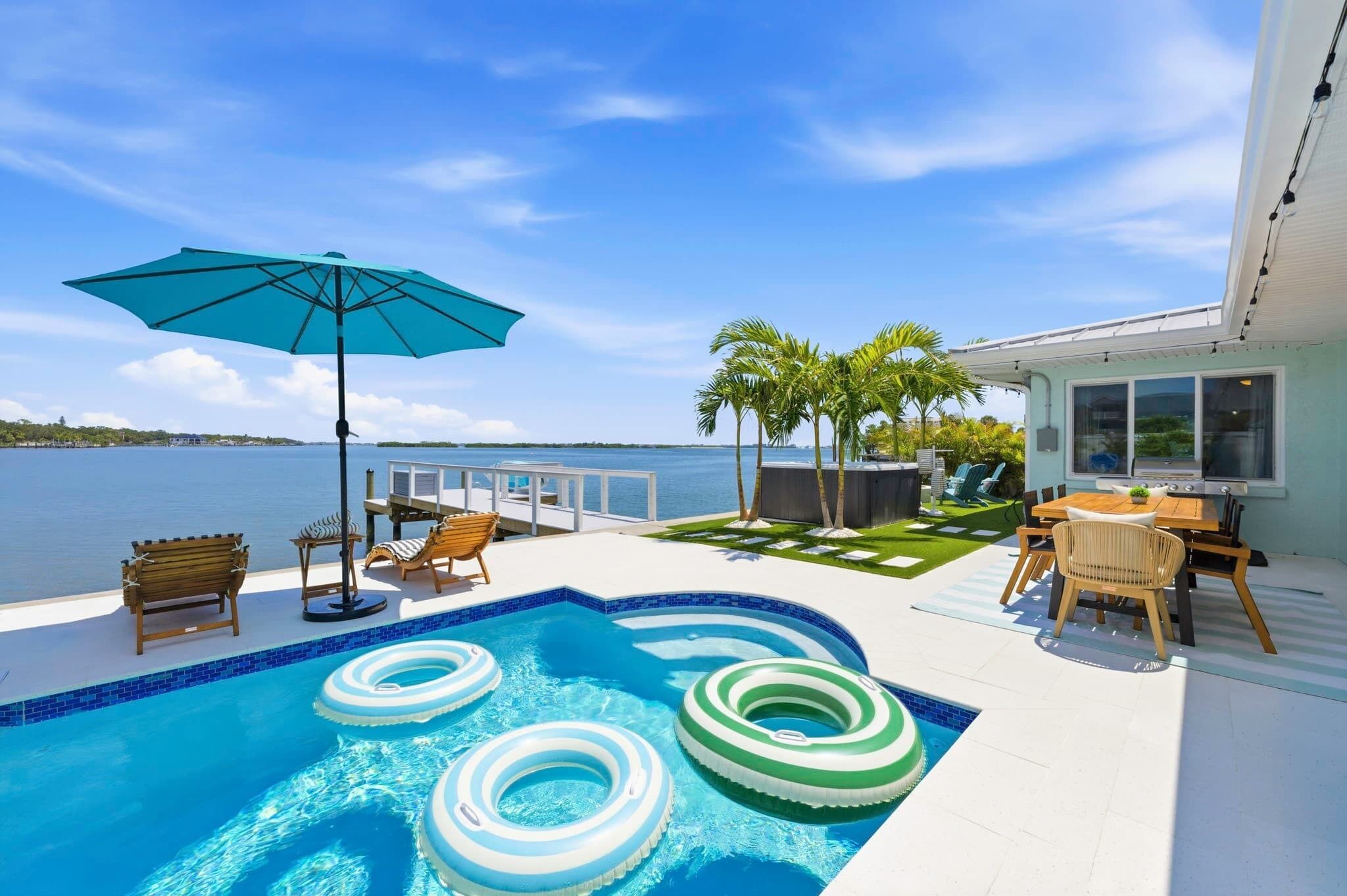 A swimming pool with inflatable rings, a table with chairs, and a view of the sea.