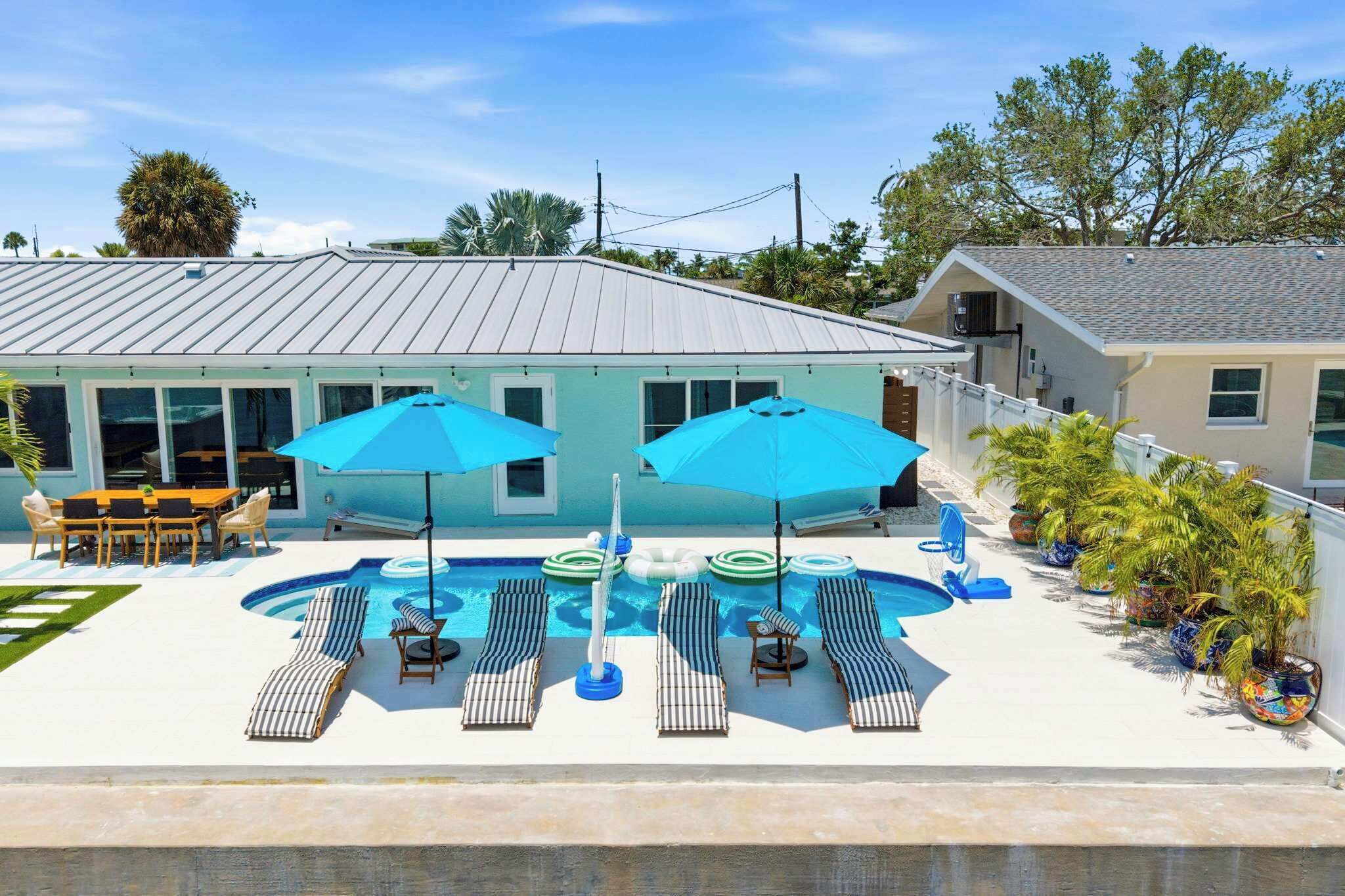 A pool area with lounge chairs and umbrellas, a covered seating area, and a building with a light blue exterior.