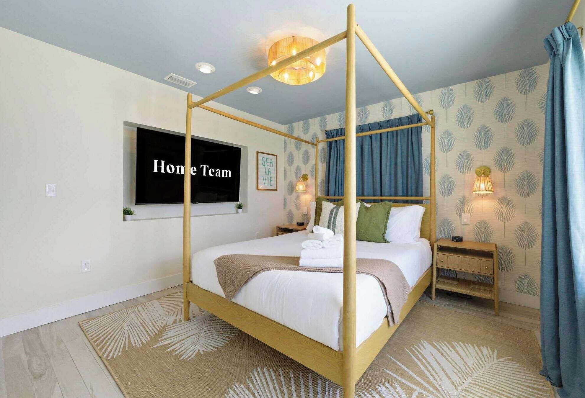 A bedroom with a four-poster bed, a flat-screen TV, a bedside table with a lamp, and a patterned wall.