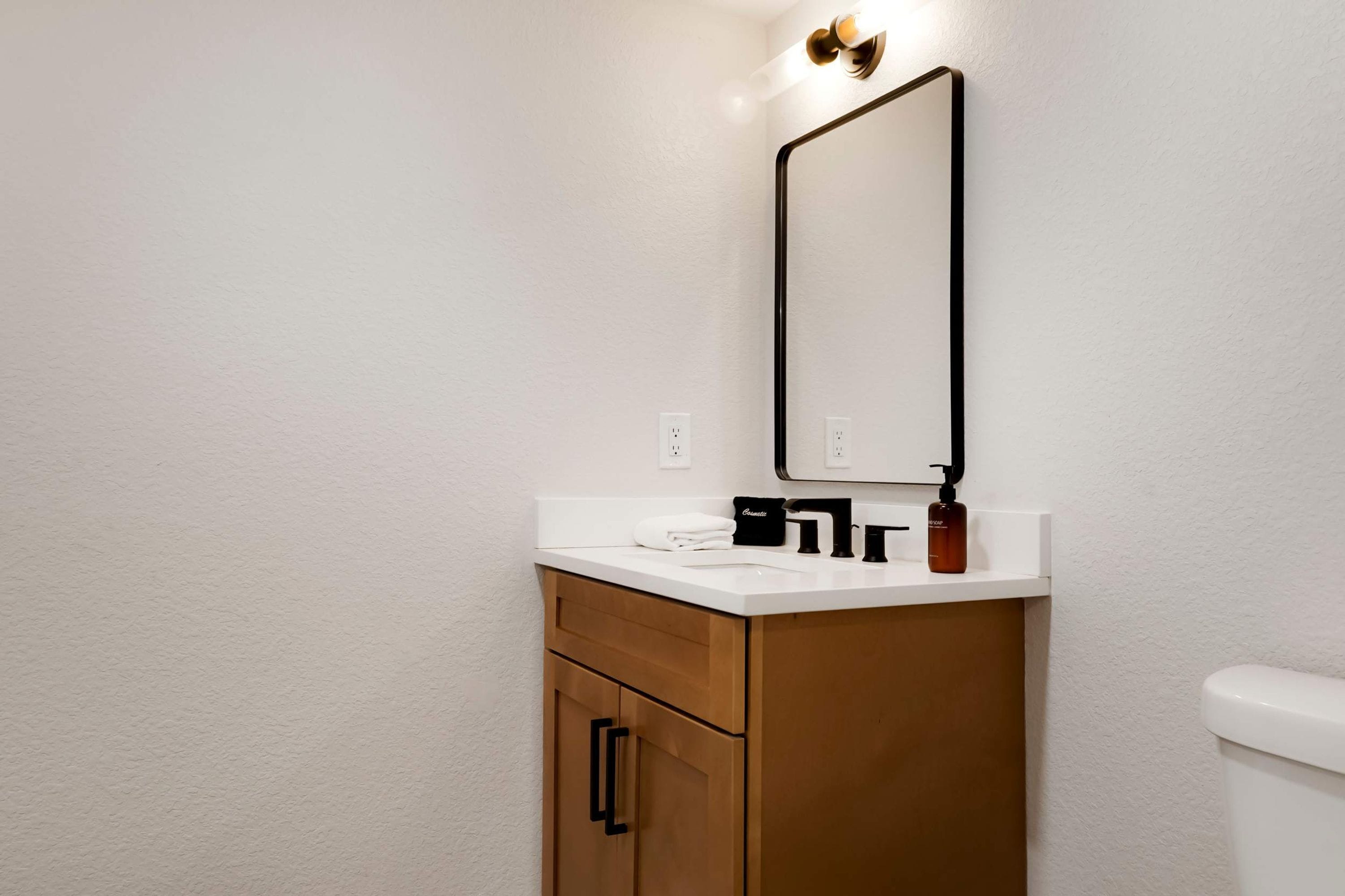 A bathroom with a white countertop, a mirror, a sink, a toilet, and a cabinet with a towel holder.
