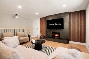 A modern living room with a sofa, a coffee table, a fireplace, and a TV mounted on the wall. - Peak State Hot Tub Sauna Arcade (Littleton)