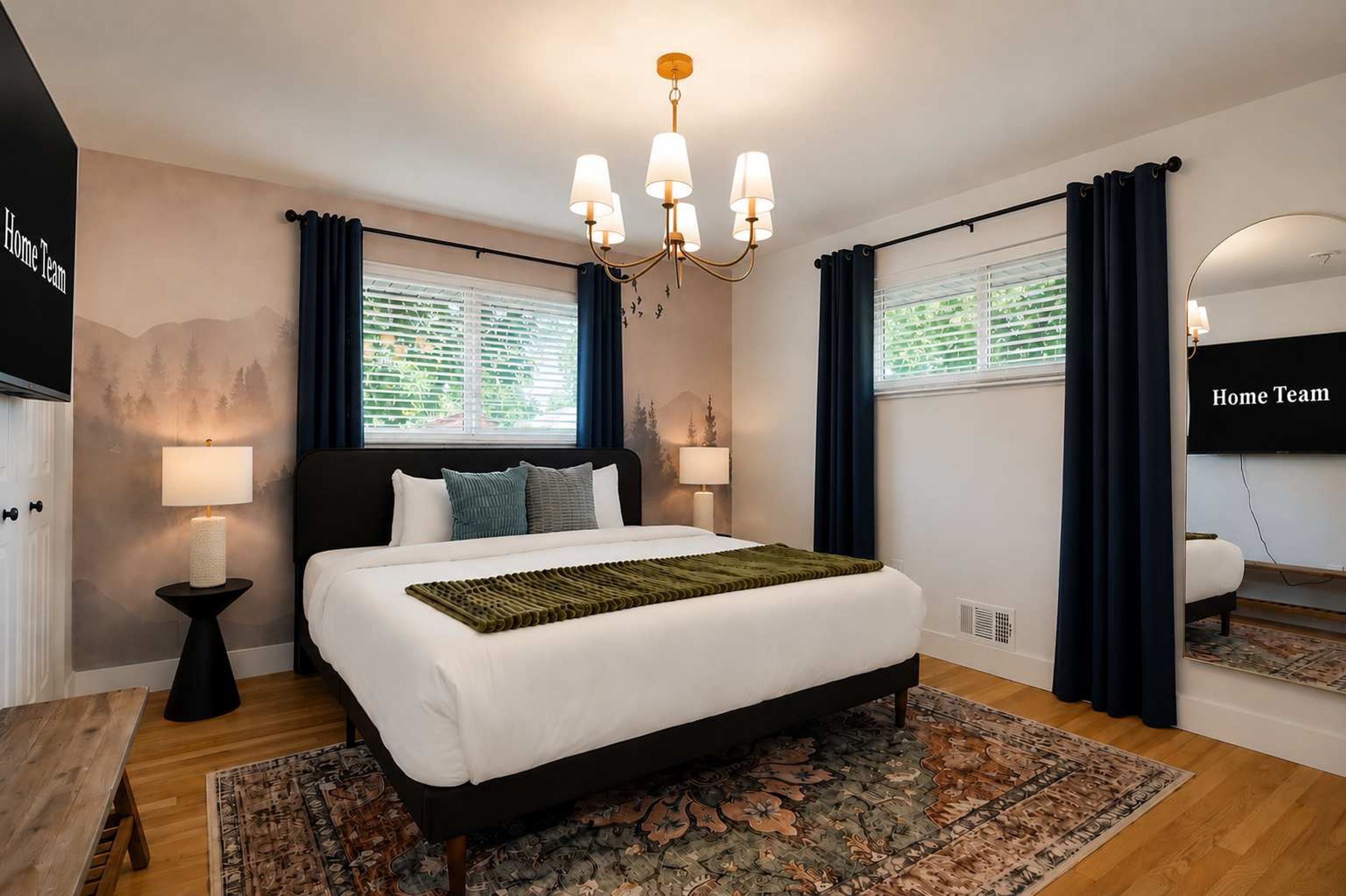 A bedroom with a large bed, a chandelier, a window with curtains, and a wall-mounted TV.