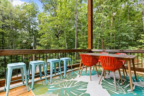 Une terrasse en bois avec une table et des chaises, entourée d’une forêt.
