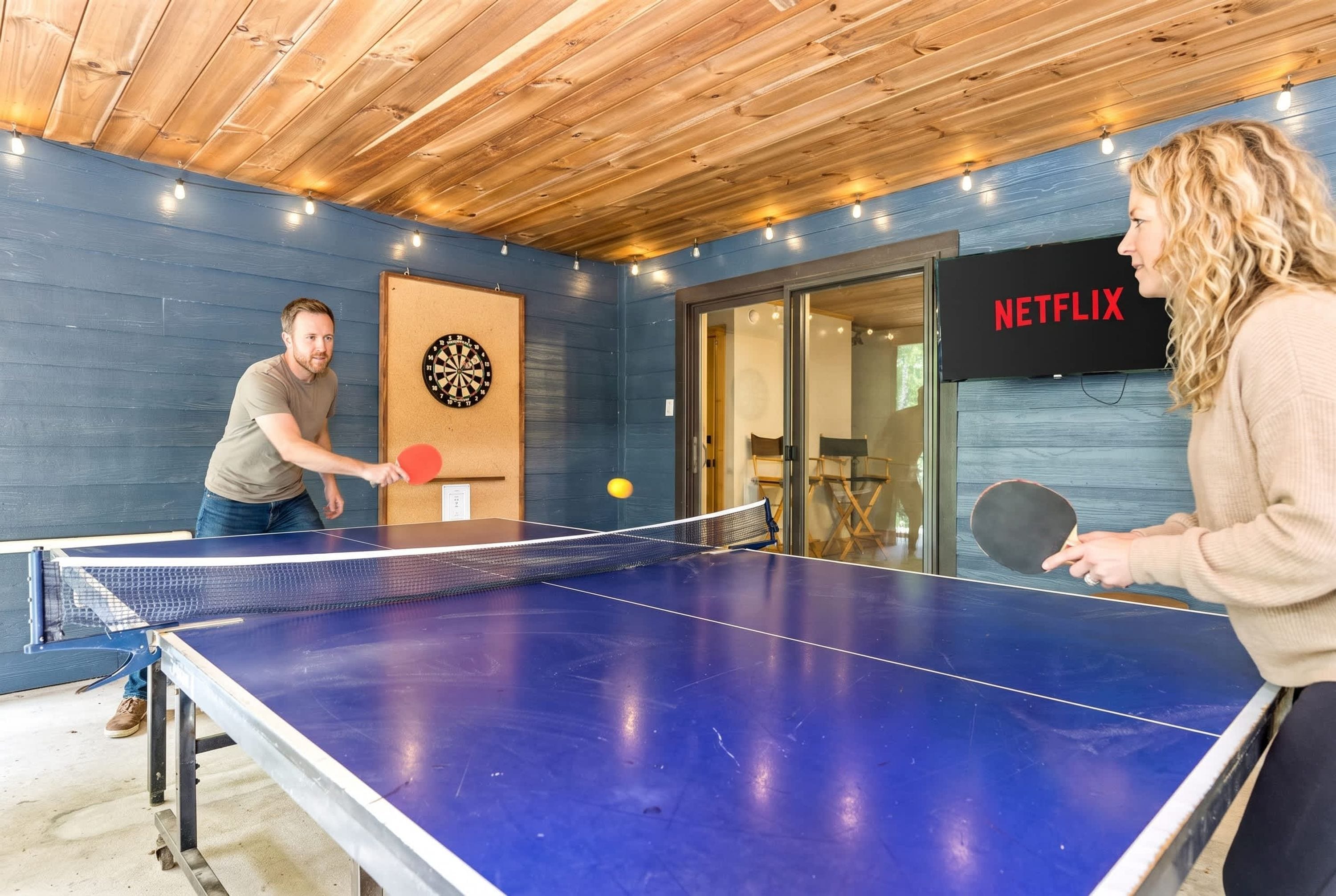 A ping pong table in a room with a dartboard and a sign indicating a Netflix service.
