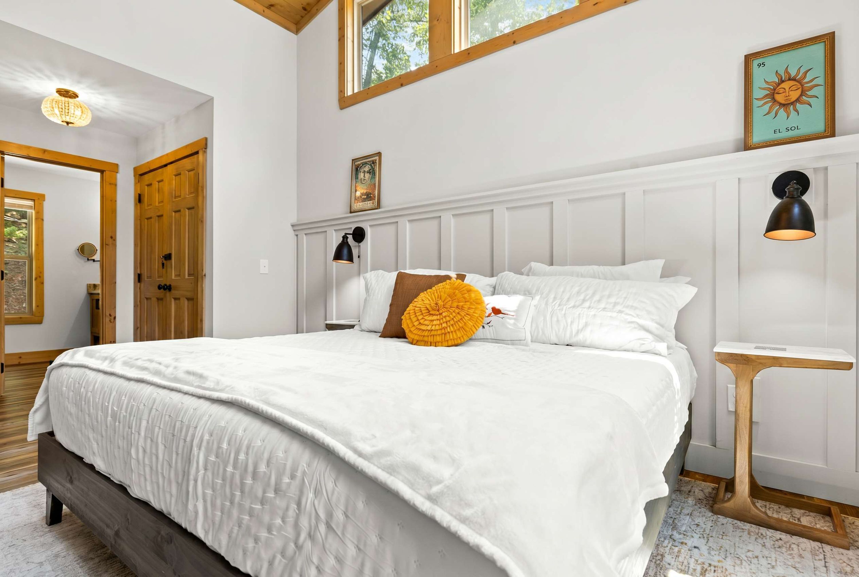 Un dormitorio con una cama grande, cabecera de madera, mesita de noche, lámpara de pared e imagen enmarcada.