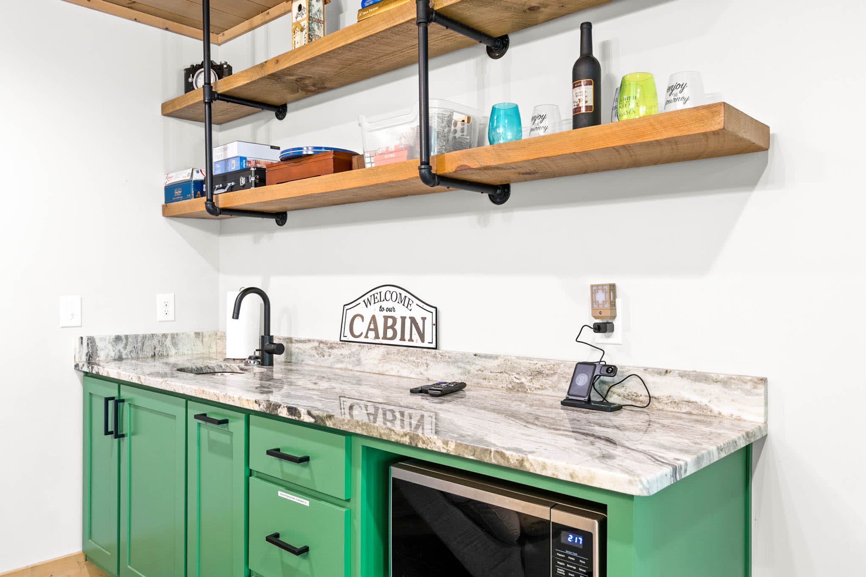 Una cocina con armarios verdes, encimera de mármol y un cartel que dice 'BIENVENIDO a nuestra CABAÑA'.