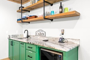 A kitchen with green cabinets, a marble countertop, and a sign that reads 'WELCOME to our CABIN.'
