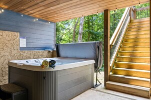 A hot tub with a towel and a chair, a wooden staircase, and a wooden ceiling with hanging lights.