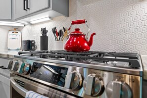 Une cuisine équipée d’une cuisinière en acier inoxydable, d’une bouilloire rouge et d’un porte-ustensiles contenant divers accessoires de cuisine.