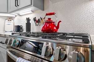 Una cocina con estufa de acero inoxidable, un hervidor rojo y un recipiente con diferentes utensilios de cocina.