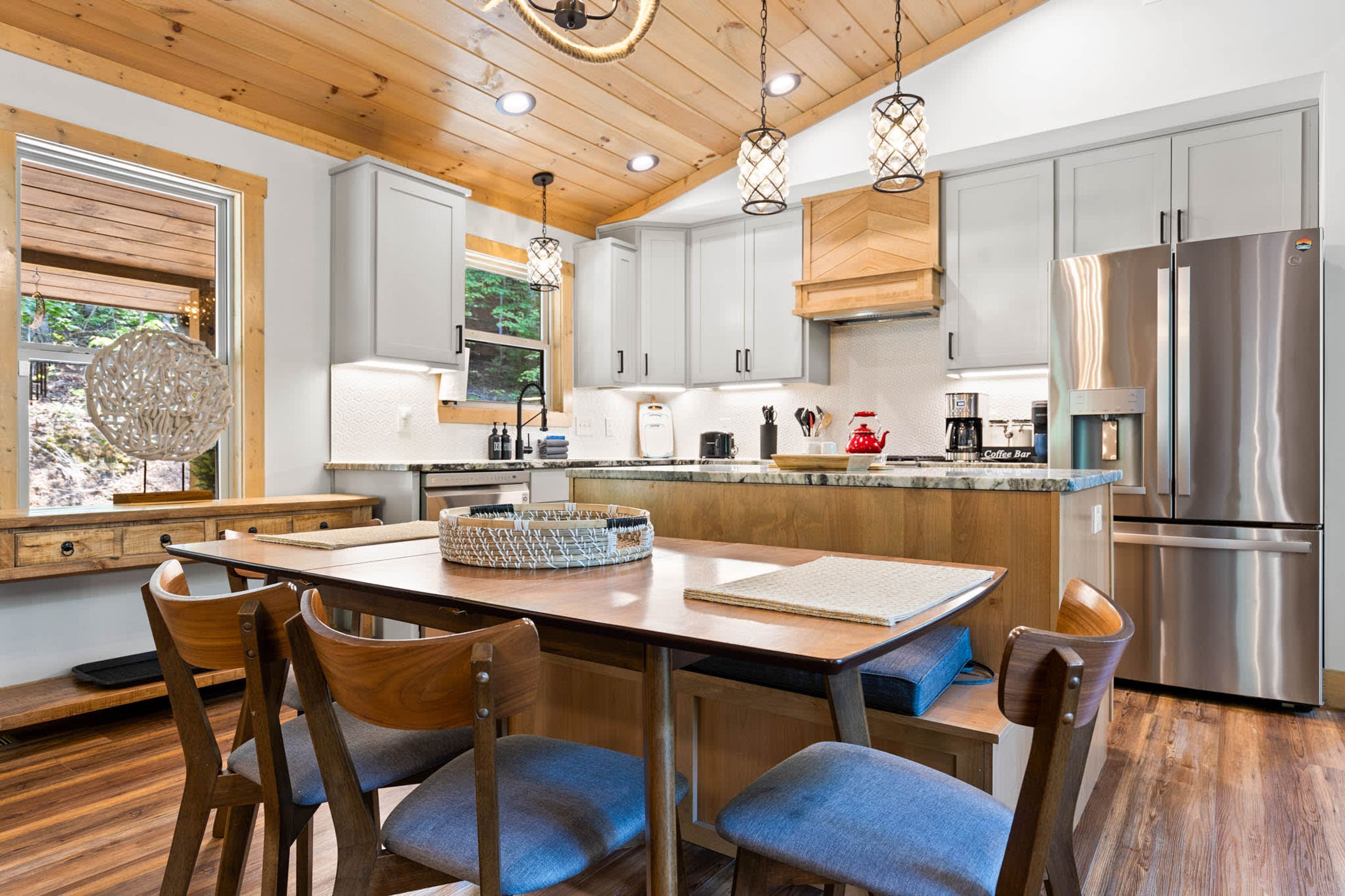 Een moderne keuken met houten kasten, een koelkast van roestvrij staal, en een eethoek met een houten tafel en stoelen.
