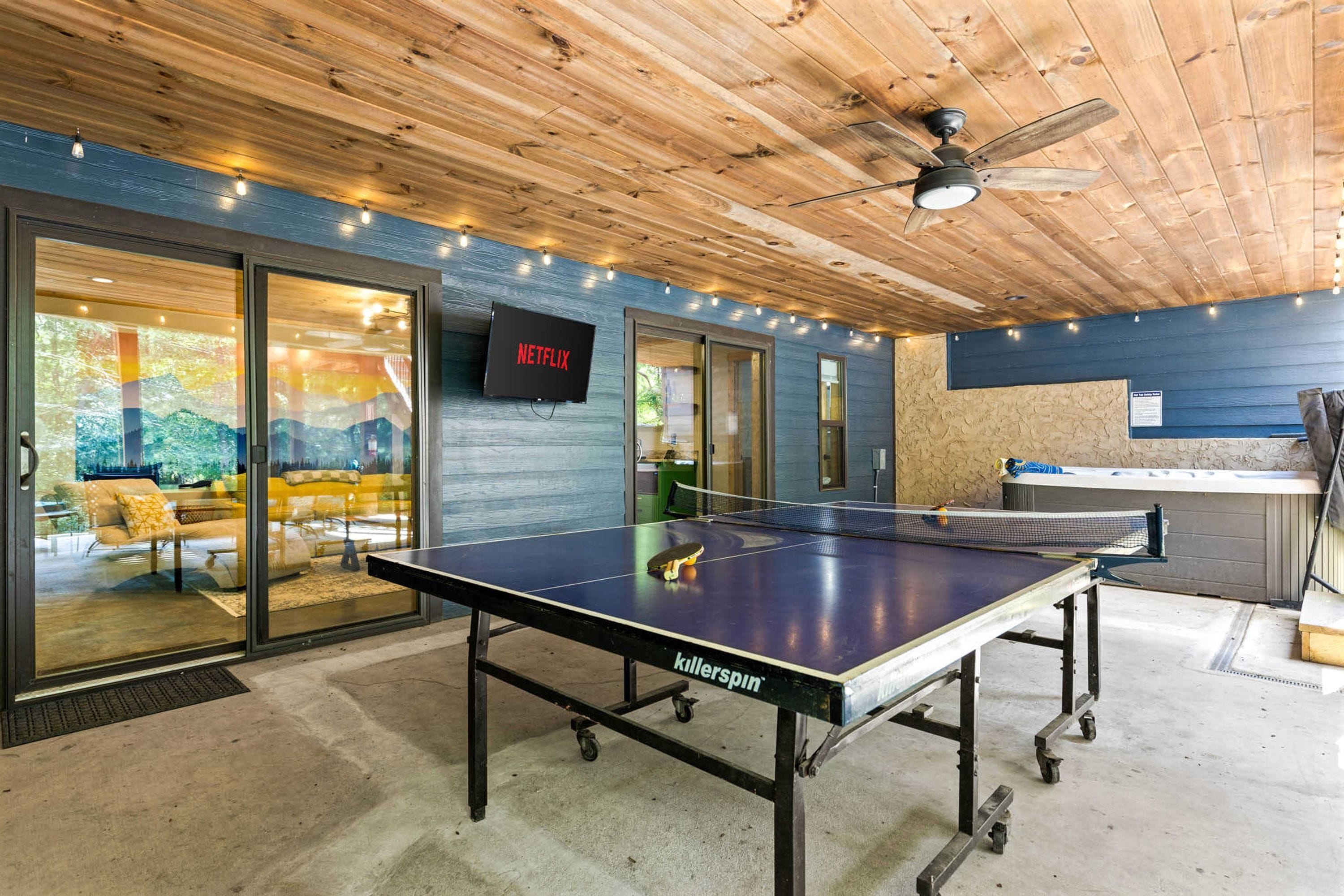 Una mesa de ping pong con ruedas, un ventilador de techo y un televisor mostrando el logotipo de Netflix.
