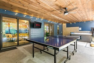 Una mesa de ping pong con ruedas, un ventilador de techo y un televisor mostrando el logotipo de Netflix.