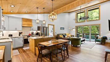 Una cocina amplia con electrodomésticos modernos, un comedor con mobiliario de madera y una sala de estar con un gran ventanal con vistas a la vegetación.