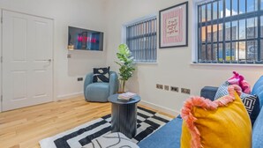 A living room with a sofa, a coffee table, a plant, a wall-mounted TV, and a window with blinds. - Stylish 2BR Apt Near City Centre - 2 Ensuites Wifi (Birmingham)