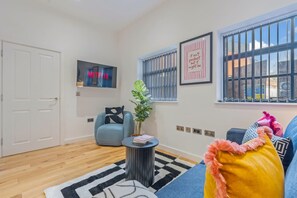 Ein Wohnzimmer mit einer Couch, einem Couchtisch, einer Pflanze, einem Wandfernseher und einem Fenster mit Jalousien.