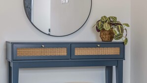 A room with a round mirror, a dark blue console table with wicker baskets, and a grey ottoman. - Stylish 2BR Apt Near City Centre - 2 Ensuites Wifi (Birmingham)