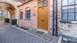 A brick building with a wooden door, windows, and a small outdoor area with a paved walkway. - Stylish 2BR Apt Near City Centre - 2 Ensuites Wifi (Birmingham)