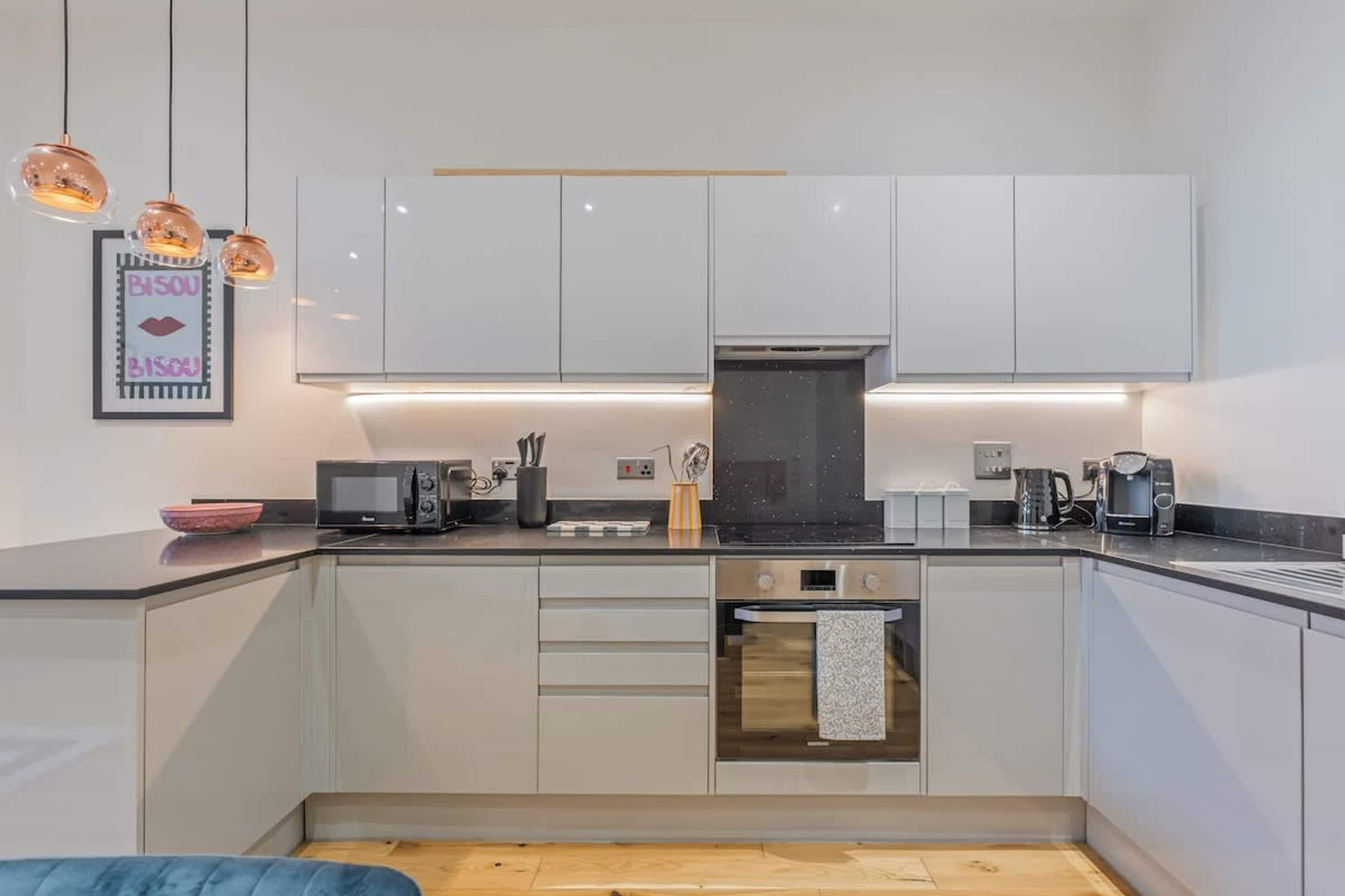 Une cuisine moderne avec des meubles blancs, un four à micro-ondes, une bouilloire et un grille-pain.