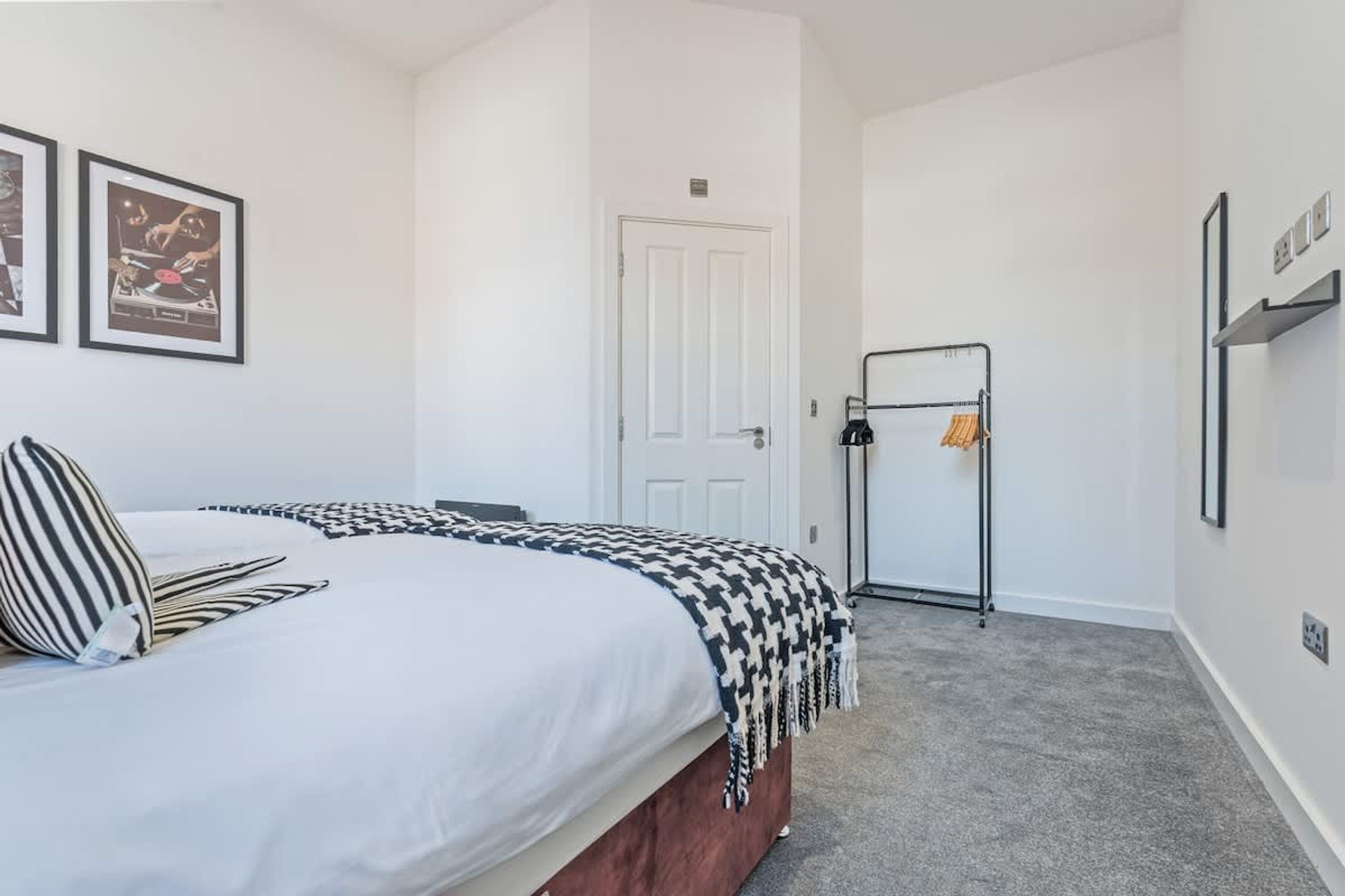 A bedroom with a bed, a door, a coat rack, and framed pictures on the wall.