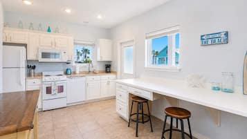 A kitchen with white cabinets, a stove, a microwave, and a window with a view of a blue building.