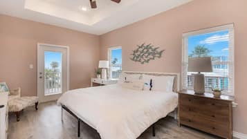 A bedroom with a bed, a nightstand, a dresser, a ceiling fan, a window with a view, and a door.