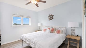 A bedroom with a bed, a ceiling fan, a window, a wall clock, and bedside lamps.
