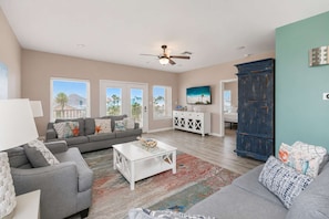 A spacious living room with a grey sofa, white coffee table, and a blue cabinet. - Pier Pressure Pools Beach Access Sunset View (Port Aransas)
