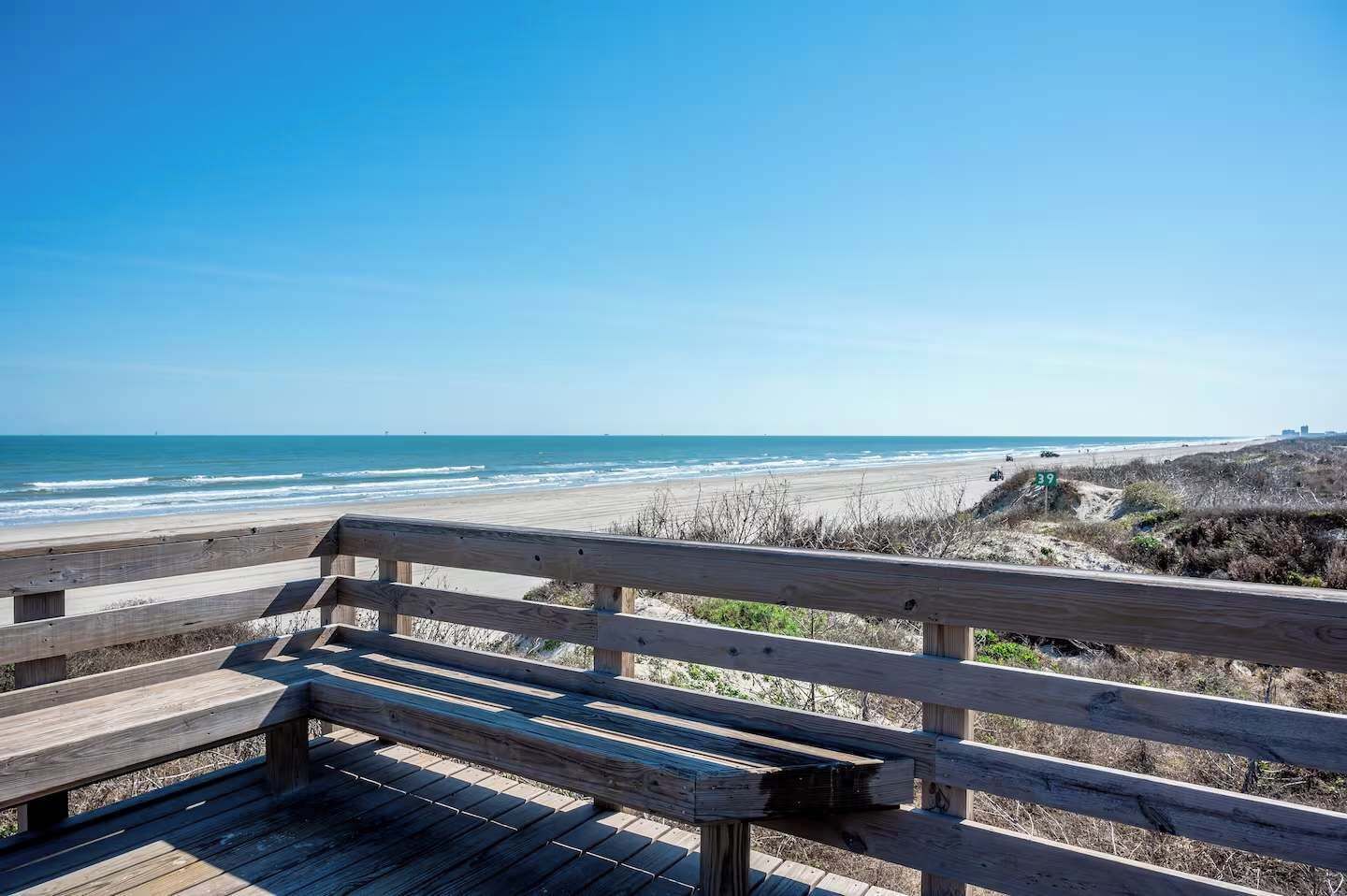 A wooden bench overlooking a beach with a clear view of the ocean and a road sign indicating route 39.