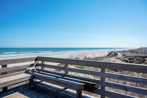 A wooden bench overlooking a beach with a clear view of the ocean and a road sign indicating route 39. - Pier Pressure Pools Beach Access Sunset View (Port Aransas)