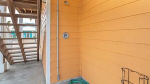 A corner of a room with wooden walls, a metal pipe, and a green hose. - Pier Pressure Pools Beach Access Sunset View (Port Aransas)