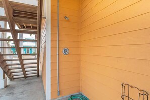 A corner of a room with wooden walls, a metal pipe, and a green hose. - Pier Pressure Pools Beach Access Sunset View (Port Aransas)